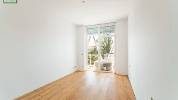 Heller, unmöblierter Raum mit Holzboden, weißen Wänden und Zugang zu einem Balkon.