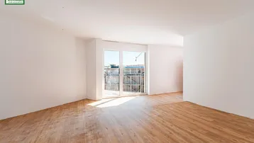 Leerer Raum mit hellem Parkettboden und großen Fenstern, die auf einen Balkon führen.
