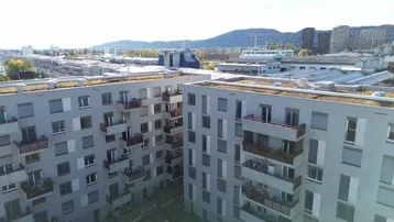 Luftaufnahme einer modernen Wohnanlage mit Balkonen und Blick auf die Stadt und Berge.