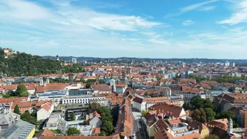 Weitläufiger Blick über die Dächer der Stadt Graz mit dem Schlossberg im Hintergrund.