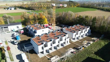Luftaufnahme der Reihenhäuser im Bau mit Baukran und ländlicher Umgebung, umgeben von Feldern.