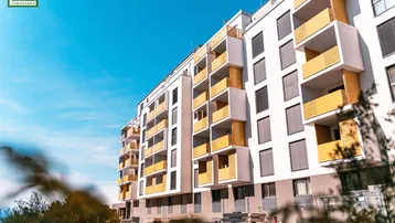 Moderne Wohnanlage mit weißer Fassade und gelben Balkonen unter blauem Himmel.