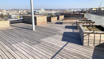 Große Dachterrasse mit Holzboden und Pflanzbeeten, bietet weiten Stadtblick.