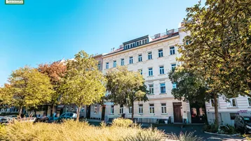 Historisches Wohngebäude mit klassischer Fassade und begrüntem Vorgarten unter blauem Himmel.