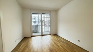 Leerer Raum mit Parkettboden und großen Fenstern, die viel Tageslicht hereinlassen.