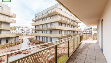 Langer Balkon mit Fliesenboden und Blick auf moderne Wohngebäude in der Umgebung.
