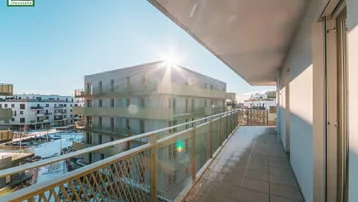 Langer, sonniger Balkon mit Fliesenboden und Metallgeländer, bietet Blick auf die Umgebung.