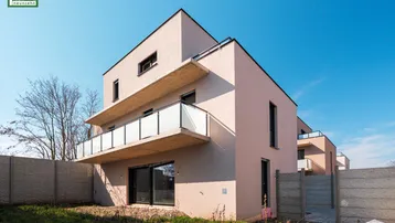 Modernes Reihenhaus mit Balkonen und Gartenbereich im Bau unter blauem Himmel.