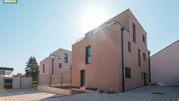 Moderne Neubauten mit heller Fassade unter strahlendem Sonnenschein und gepflastertem Vorplatz.