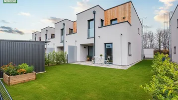 Moderne Reihenhäuser mit gepflegtem Rasen und kleiner Terrasse im Gartenbereich.