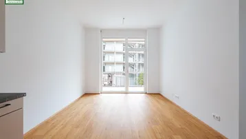 Helles, leeres Zimmer mit Holzboden und Zugang zu einem französischen Balkon.