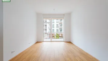 Heller Raum mit Laminatboden und Zugang zu einem französischen Balkon.