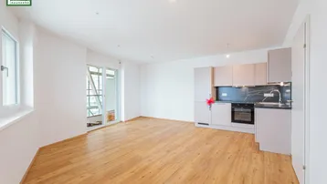 Heller offener Wohnbereich mit integrierter Küche, Parkettboden und Zugang zum Balkon.