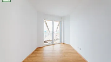 Helles, leeres Zimmer mit Parkettboden und Zugang zu einem französischen Balkon.