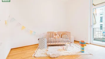 Kinderzimmer mit Babybett, Spielzeug, Holzboden und Zugang zu einem französischen Balkon.