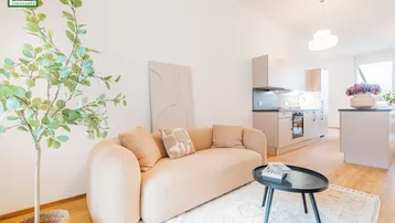 Heller offener Wohnbereich mit beigem Sofa, Holzboden und integrierter moderner Küche.