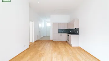 Heller Wohnbereich mit Holzboden und einer modernen Küchenzeile im Hintergrund.