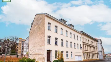 Ansicht der modernen Gebäudefassade mit hell gestrichenen Wänden und großen Fenstern an einer Straßenecke.