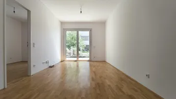 Helles, leeres Wohnzimmer mit Parkettboden und Zugang zur Terrasse oder zum Garten.