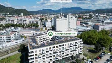 Luftaufnahme eines modernen Wohngebäudes mit Solaranlagen auf dem Dach und umliegender Infrastruktur.