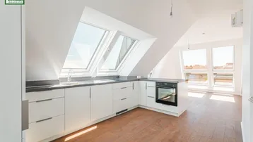 Helle Dachgeschossküche mit modernen weißen Schränken, integriertem Backofen und Dachfenstern.
