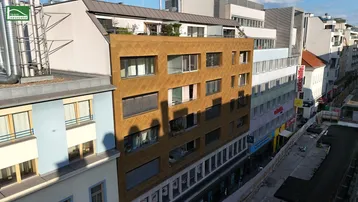 Moderne Fassade eines Mehrfamilienhauses mit markanter goldbrauner Verkleidung und vielen Fenstern in der Stadt.