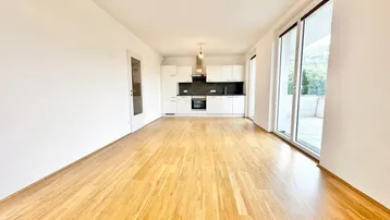 Heller, offener Wohnbereich mit integrierter Küche, Parkettboden und Zugang zu einem Balkon.