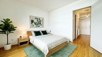 Helles Schlafzimmer mit Holzbett, Nachttischen und einem grünen Teppich, der eine gemütliche Atmosphäre schafft.