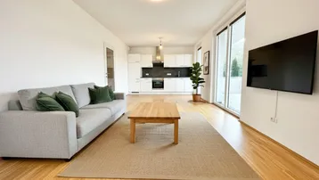 Helles, offenes Wohnzimmer mit integrierter Küche, Holzboden und Zugang zum Balkon.