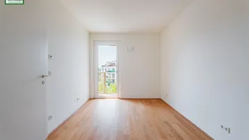 Helles Zimmer mit Holzboden und Zugang zu einem französischen Balkon.