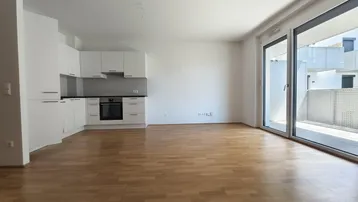 Heller offener Wohnbereich mit integrierter Küche, Parkettboden und Zugang zu einem Balkon.