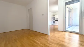 Offener Wohnbereich mit Parkettboden, hellem Ambiente und Blick zur Küche und Balkon.