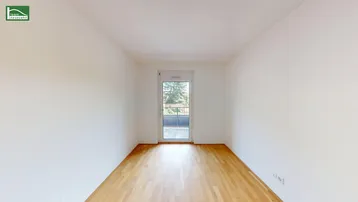 Leeres Schlafzimmer mit Holzboden und Fenstertür, die zu einem französischen Balkon führt.