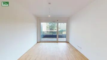 Helles, leeres Wohnzimmer mit Holzboden und Zugang zu einem Balkon.