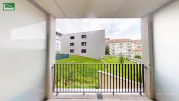 Blick von einem Balkon auf eine grüne Rasenfläche und umliegende moderne Gebäude.