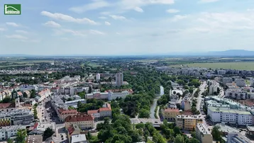 Weitläufige Luftaufnahme einer Stadt mit Fluss, Grünflächen und Bergen im Hintergrund.