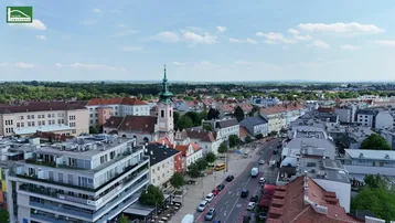 Luftaufnahme einer Stadt mit historischen Gebäuden, einer Kirche und belebten Straßen unter blauem Himmel.