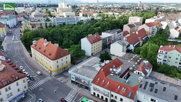 Weitläufige Luftaufnahme einer Stadtlandschaft mit verschiedenen Gebäudetypen und viel Grün.