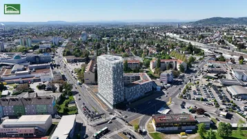 Weitläufige Luftaufnahme einer städtischen Umgebung mit einem modernen Gebäude im Zentrum und viel Grün.