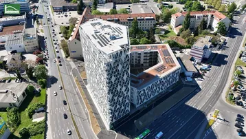 Luftaufnahme eines modernen Gebäudekomplexes mit markanter geometrischer Glasfassade und Solaranlagen in städtischer Umgebung.