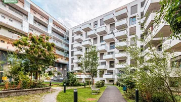Modernes Wohngebäude mit mehreren Balkonen und einem begrünten Innenhof.