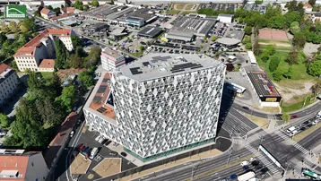 Luftaufnahme eines modernen Gebäudes mit markanter geometrischer Fassade und Solaranlagen auf dem Dach in städtischer Umgebung.