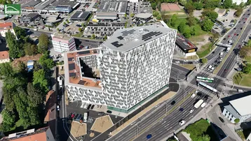 Moderne Architektur mit geometrischer Fassade und Solarpaneelen auf dem Dach, umgeben von städtischer Infrastruktur.