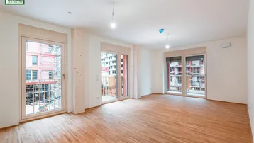 Helles, leeres Zimmer mit Holzboden und mehreren Fenstern, die zu französischen Balkonen führen.