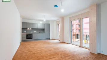 Heller Wohnbereich mit offener Küche, Holzboden und Zugang zu einem französischen Balkon.