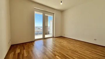 Helles Schlafzimmer mit Holzboden und Zugang zu einem Balkon, bietet viel natürliches Licht.