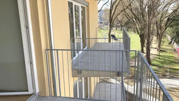Heller Balkon mit Metallgeländer und Blick auf eine Grünfläche mit Bäumen.