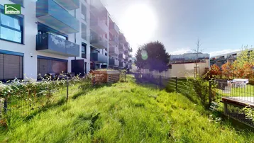 Grüne Gartenfläche vor einem modernen Wohngebäude mit Balkonen und Terrassen.
