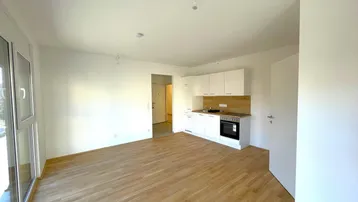 Heller Wohnbereich mit integrierter Küchenzeile, Holzboden und großem Fenster für viel Licht.