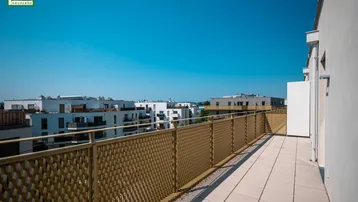 Breiter Balkon mit sonnigem Ausblick auf die umliegenden Neubauten und die Stadtlandschaft.